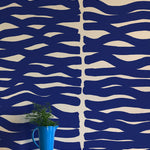A vase of flowers stands in front of a wall papered in an abstract zigzag pattern in navy on a tan field.