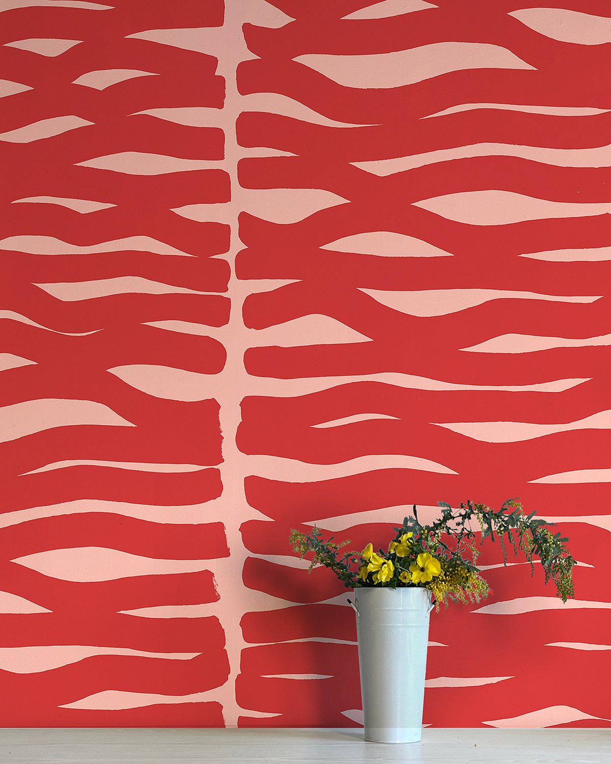 A vase of flowers stands in front of a wall papered in an abstract zigzag pattern in red on a light pink field.