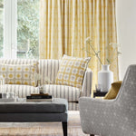 Living room scene with grey and cream upholsterd chair and coach with yellow throw pillows and a yellow printed curtain 