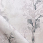 Detail of draped fabric yardage in a watercolor tree print in shades of light gray and pink on a cream field.
