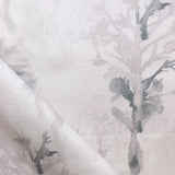 Detail of draped fabric yardage in a watercolor tree print in shades of light gray and pink on a cream field.