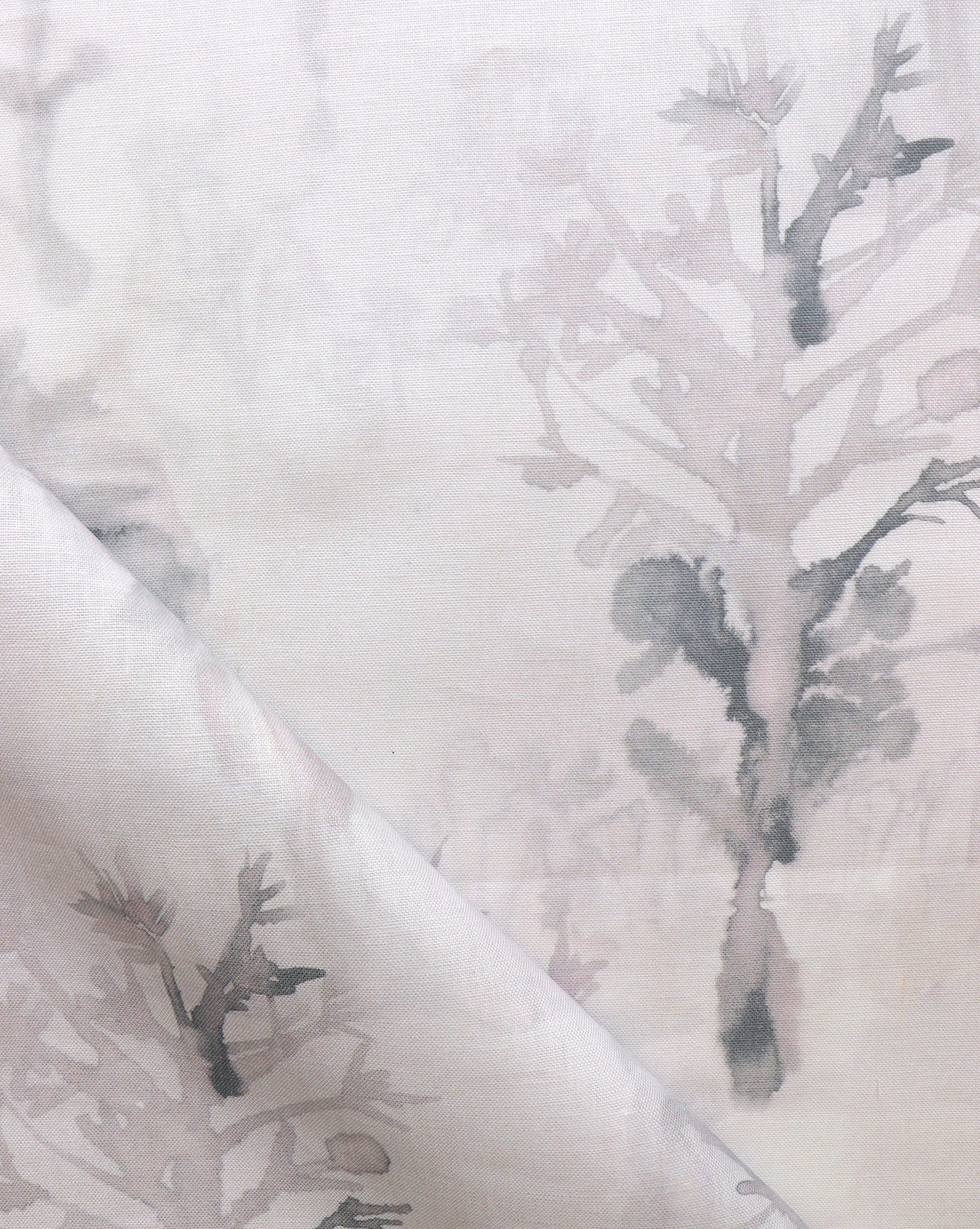 Detail of draped fabric yardage in a watercolor tree print in shades of light gray and pink on a cream field.