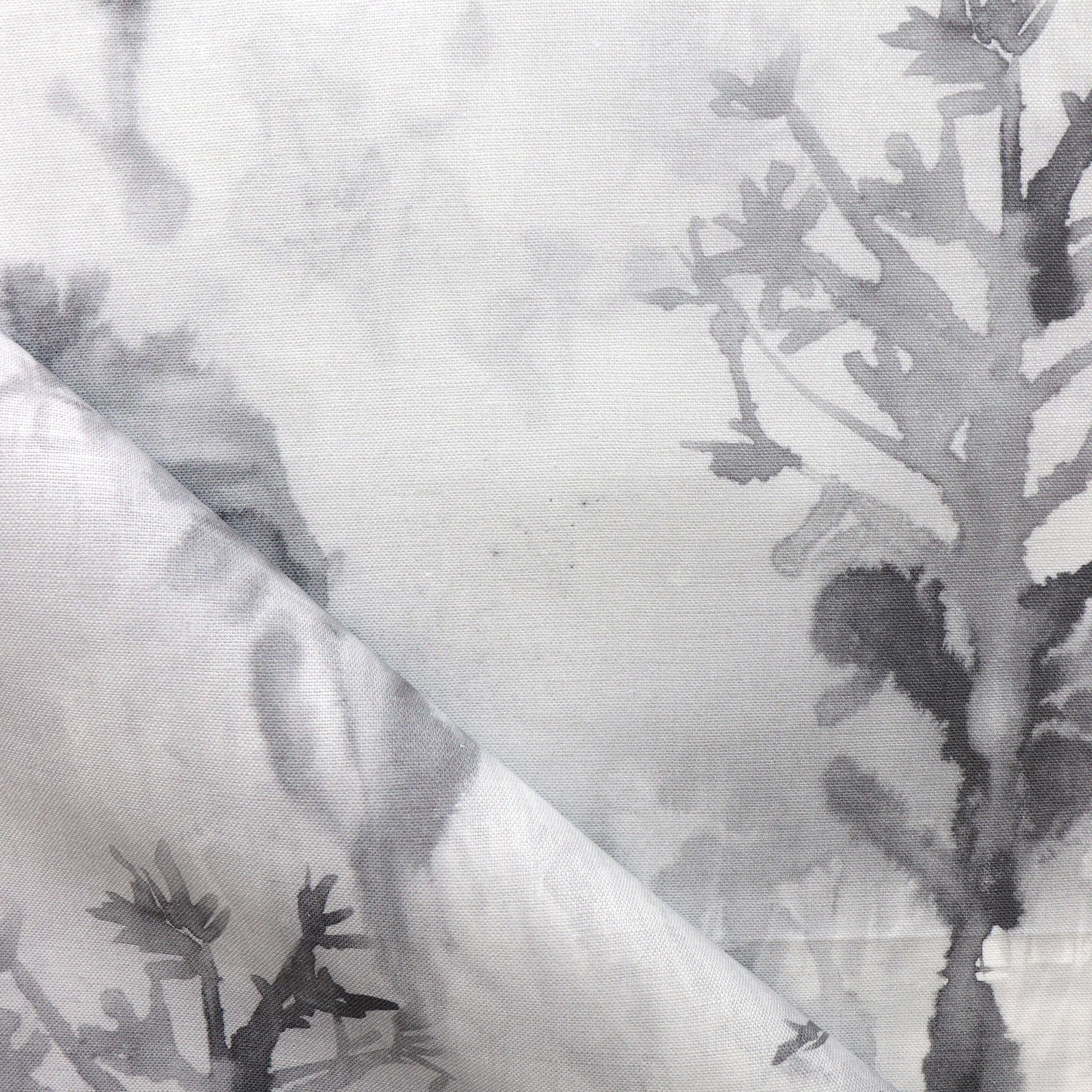 Detail of draped fabric yardage in a watercolor tree print in shades of gray and black on a white field.