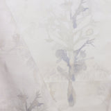 Detail of draped fabric yardage in a watercolor tree print in shades of tan and gray on a white field.