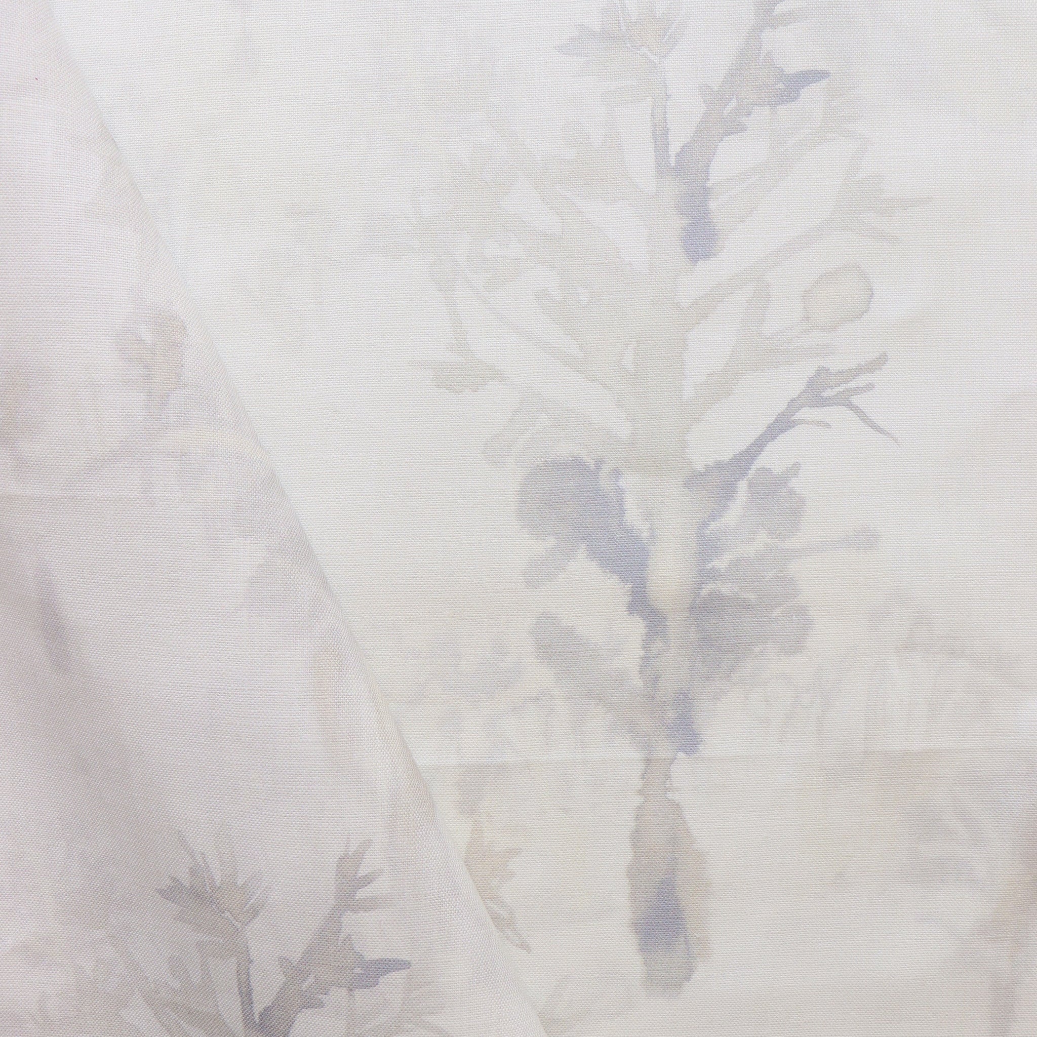 Detail of draped fabric yardage in a watercolor tree print in shades of tan and gray on a white field.