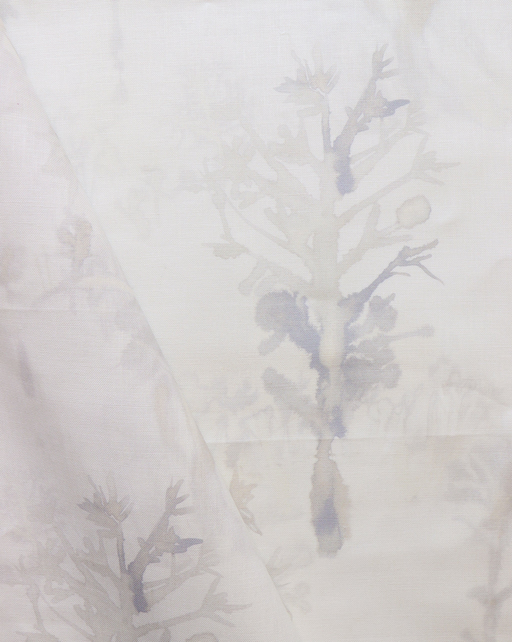 Detail of draped fabric yardage in a watercolor tree print in shades of tan and gray on a white field.