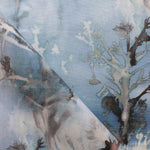 Detail of draped fabric yardage in a watercolor tree print in shades of gray and turquoise on a blue field.