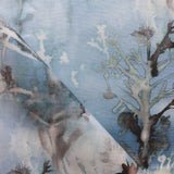Detail of draped fabric yardage in a watercolor tree print in shades of gray and turquoise on a blue field.