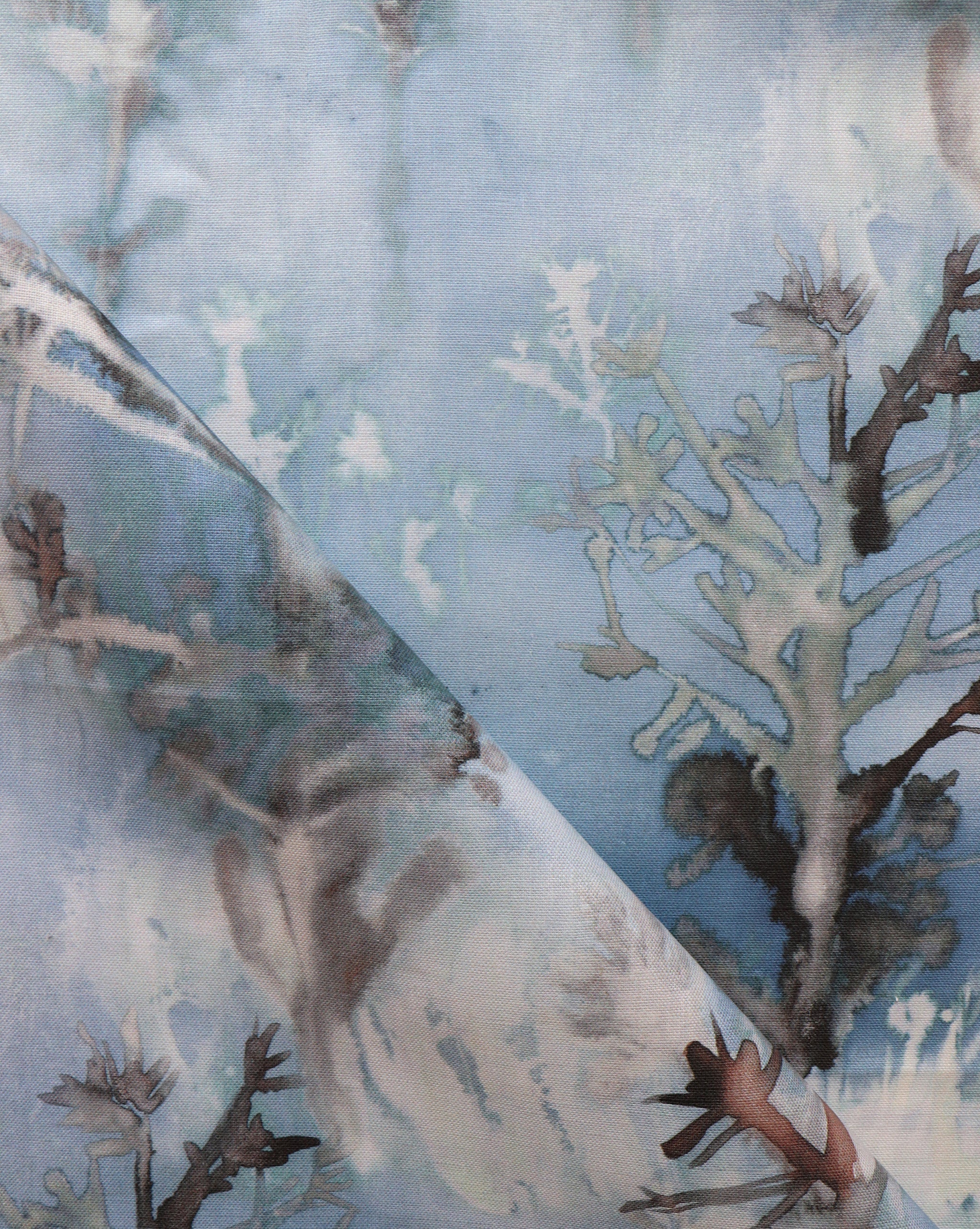 Detail of draped fabric yardage in a watercolor tree print in shades of gray and turquoise on a blue field.