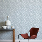 Modern brown chair and small table against a light blue floral wallpapered wall.