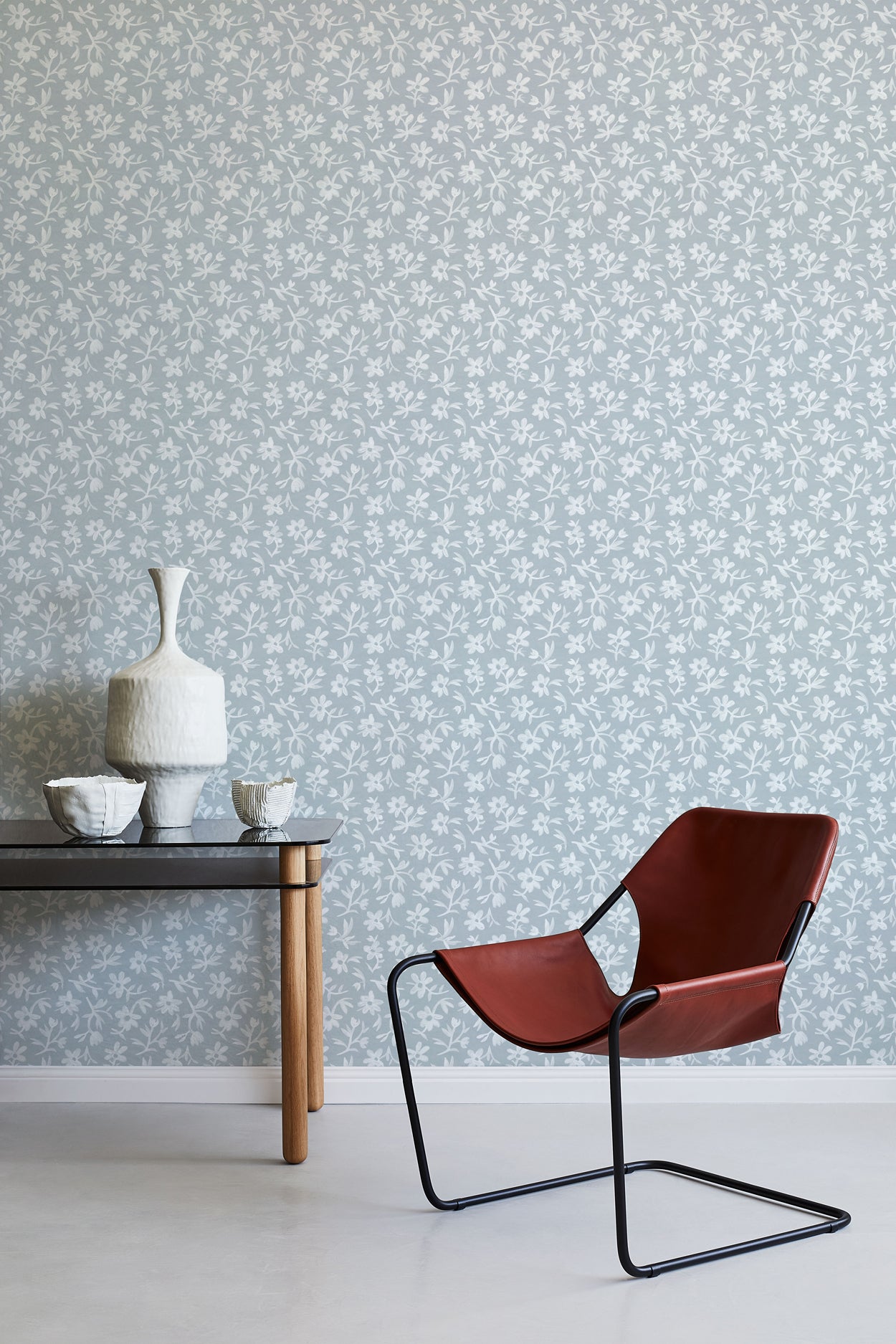 Modern brown chair and small table against a light blue floral wallpapered wall.