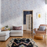 A maximalist living room tableau with walls papered in a watercolor textural print in white, purple and gray.