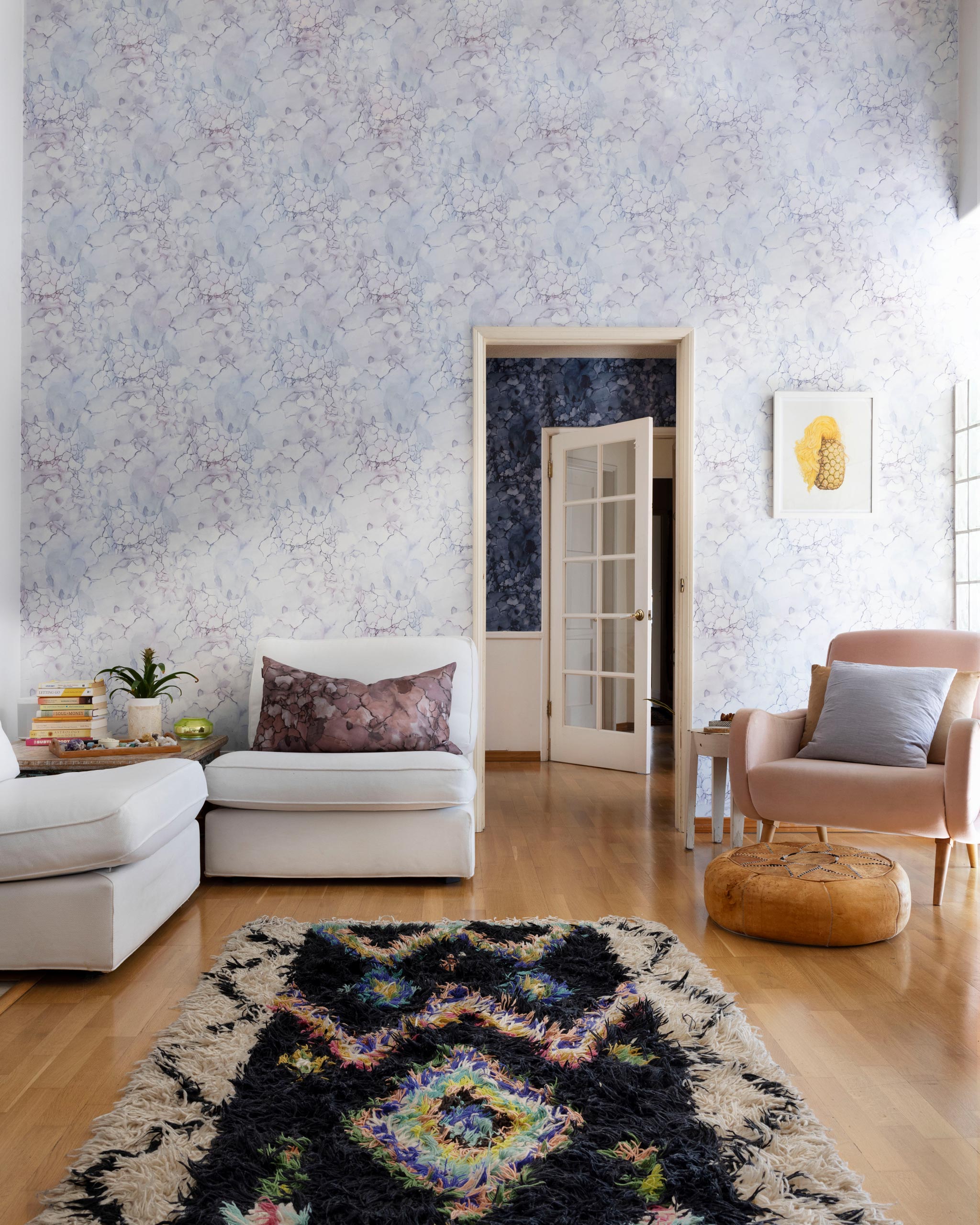 A maximalist living room tableau with walls papered in a watercolor textural print in white, purple and gray.