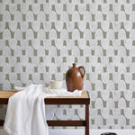 A bench with a towel and clay vases stands in front of a wall papered in an abstract scalloped print in white and olive.