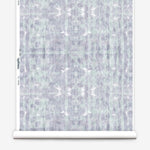 Partially unrolled wallpaper yardage in a watercolor dyed grid print in mottled purple and turquoise.