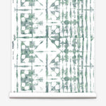 Partially unrolled wallpaper yardage in a watercolor dyed grid print in mottled white and green.