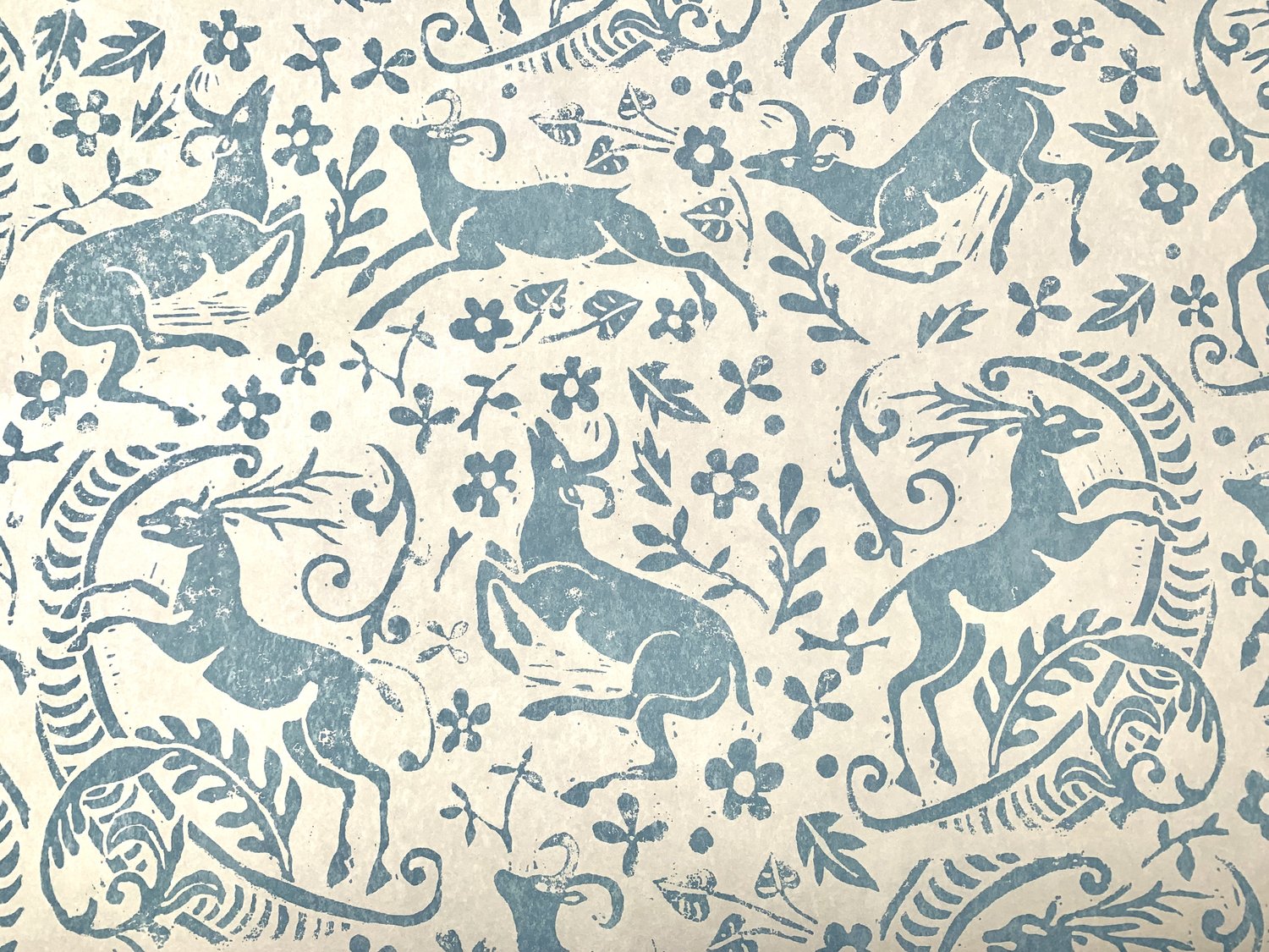 Detail of wallpaper in a deer, leaf and flower print in blue-gray on a mottled tan field.