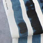 Draped crasscloth wallpaperwith bold watercolor stripes in inky blue and white on a concrete surface. 