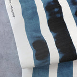 Draped crasscloth wallpaperwith bold watercolor stripes in inky blue and white on a concrete surface. 