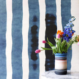 A vase of colorful tulips and flowers sits on a white marble side table against a blue and white watercolor stripe wallpaper.