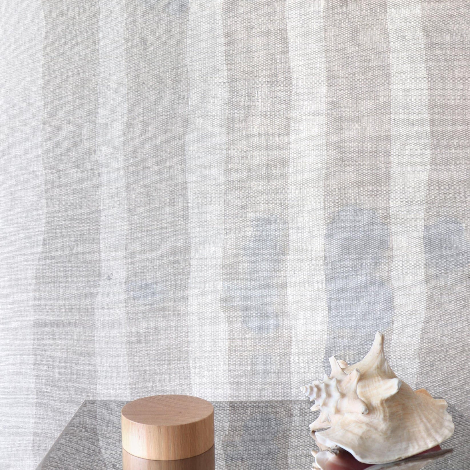 Decorative wood and steel table with conch shell against grey and cream striped grasscloth wallpaper. 