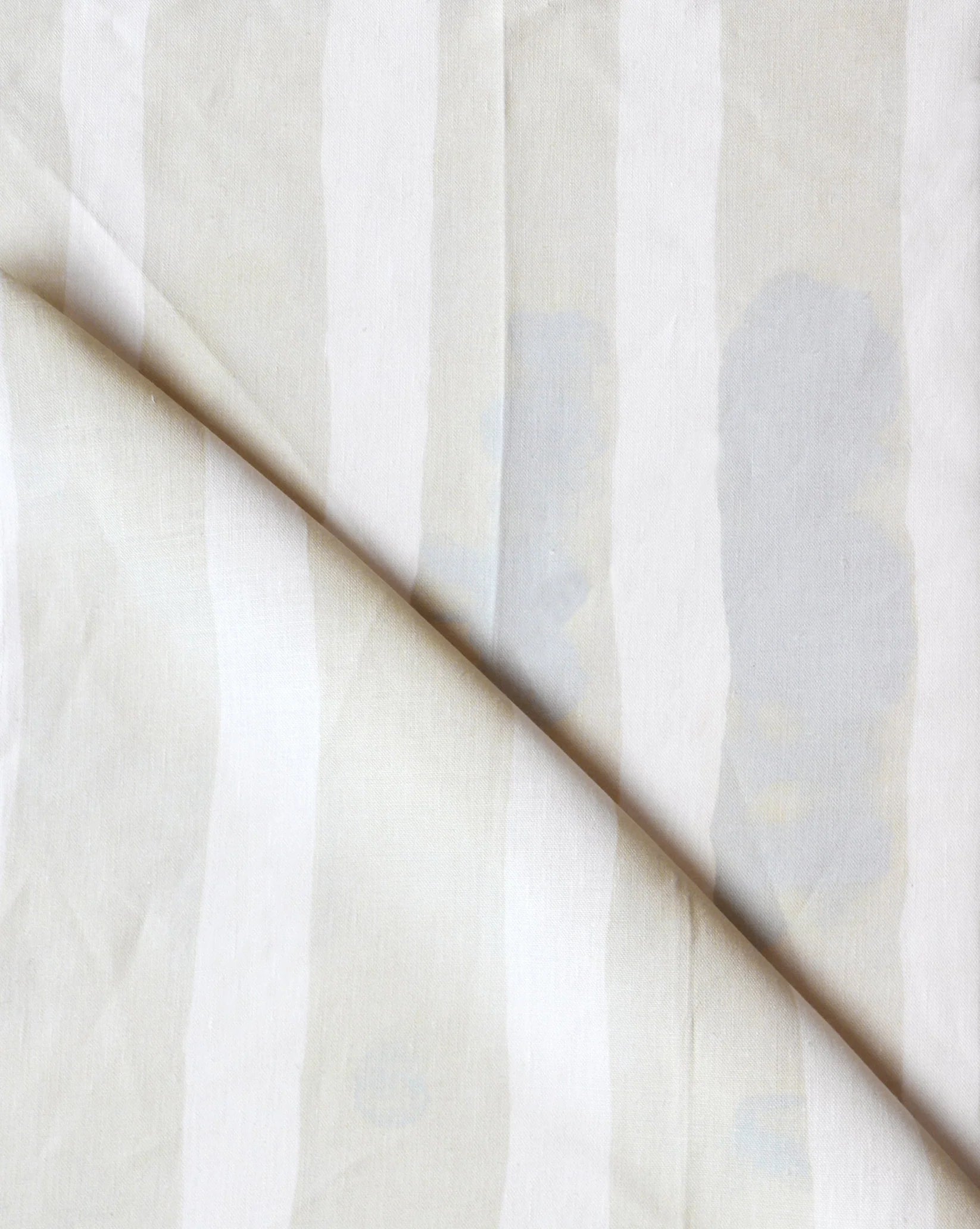Folded printed linen with bold watercolor stripes in cream and white. 