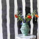 Ceramic vase on a marble table against bold black and white painted stripe wallpaper. 