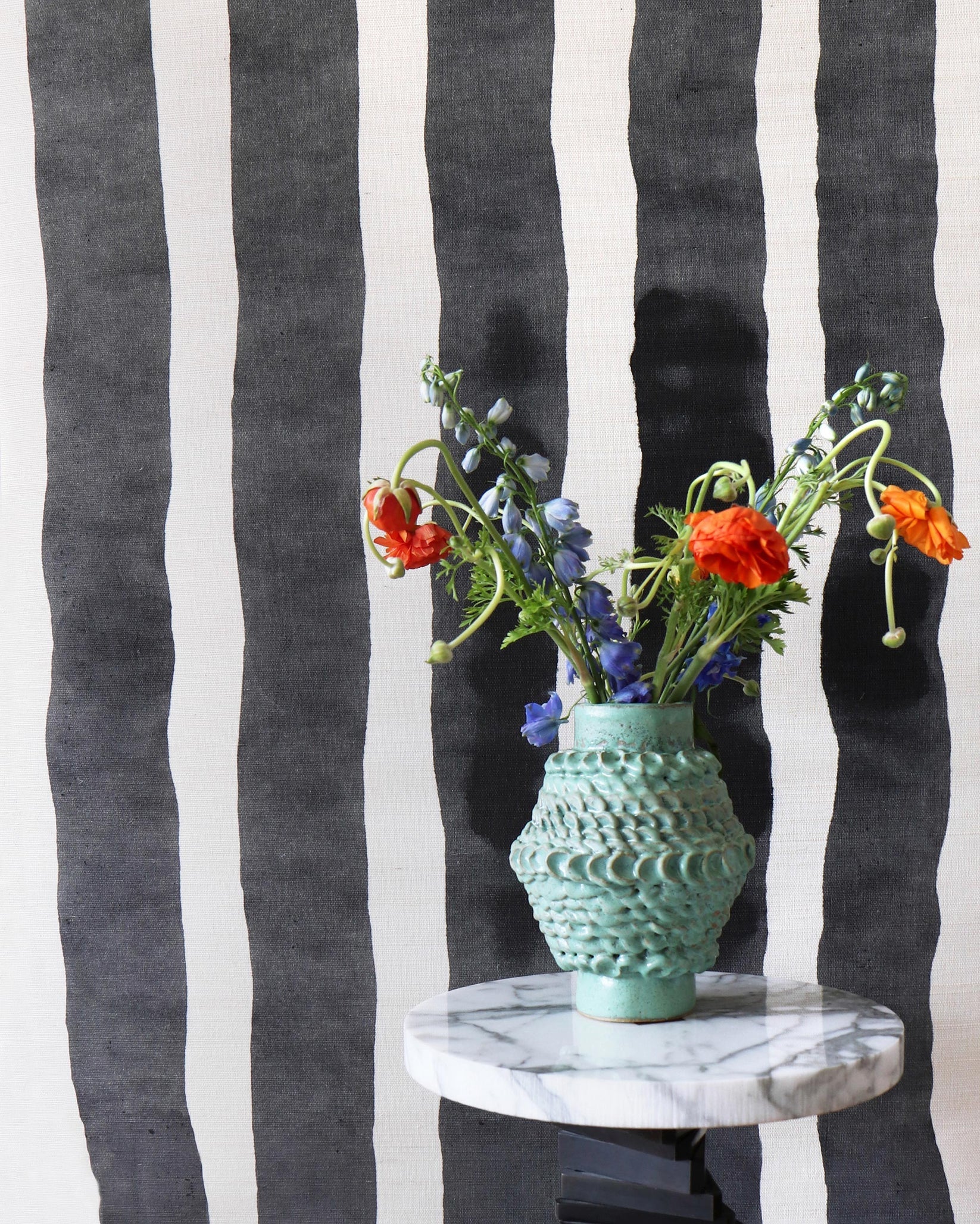Ceramic vase on a marble table against bold black and white painted stripe wallpaper. 