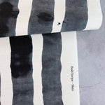 Draped length of grasscloth wallpaper with bold watercolor stripes in black and white on a concrete floor. 