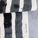Draped length of grasscloth wallpaper with bold watercolor stripes in black and white on a concrete floor. 