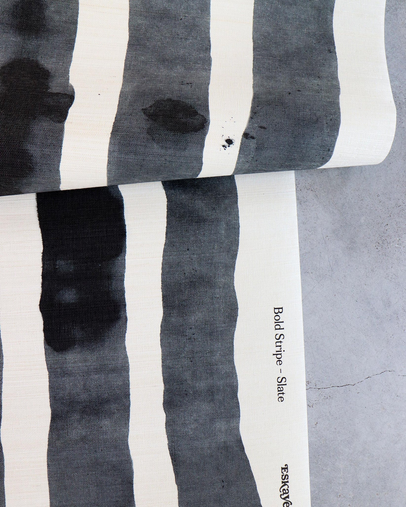 Draped length of grasscloth wallpaper with bold watercolor stripes in black and white on a concrete floor. 