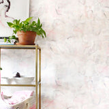 An end table with knick knacks stands in front of a wall papered in a watercolor painterly print in pastel, green and cream.