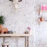 A maximalist living space with walls papered in a watercolor painterly print in shades of gray, purple and cream.