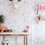 A maximalist living space with walls papered in a watercolor painterly print in shades of gray, purple and cream.