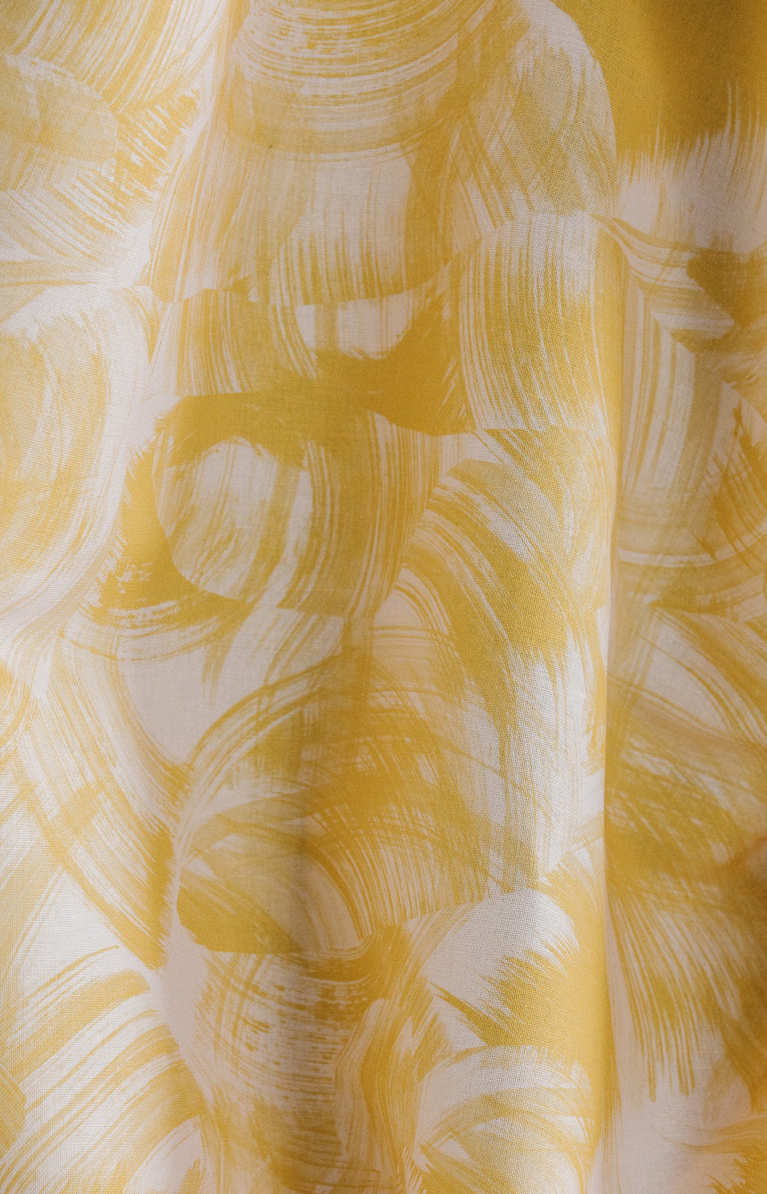 Draped fabric yardage in an absract paint swatch print in yellow on a white field.