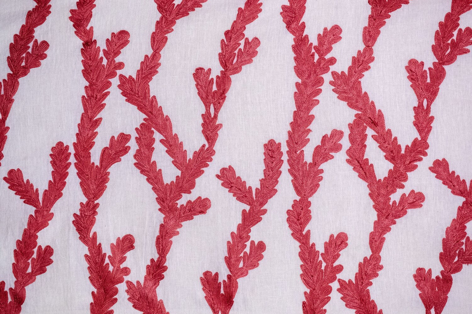 Detail of fabric in a dimensional embroidered botanical print in red on a white field.