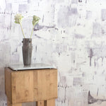 An end table with flowers stands in front of a wall papered in a watercolor textural print in shades of gray on a white field.
