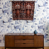 A credenza and tapestry stand in front of a wall papered in a watercolor textural print in navy, blue and white.