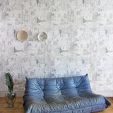 A leather sofa and plant stands in front of a wall papered in a watercolor textural print in green, pink and white.