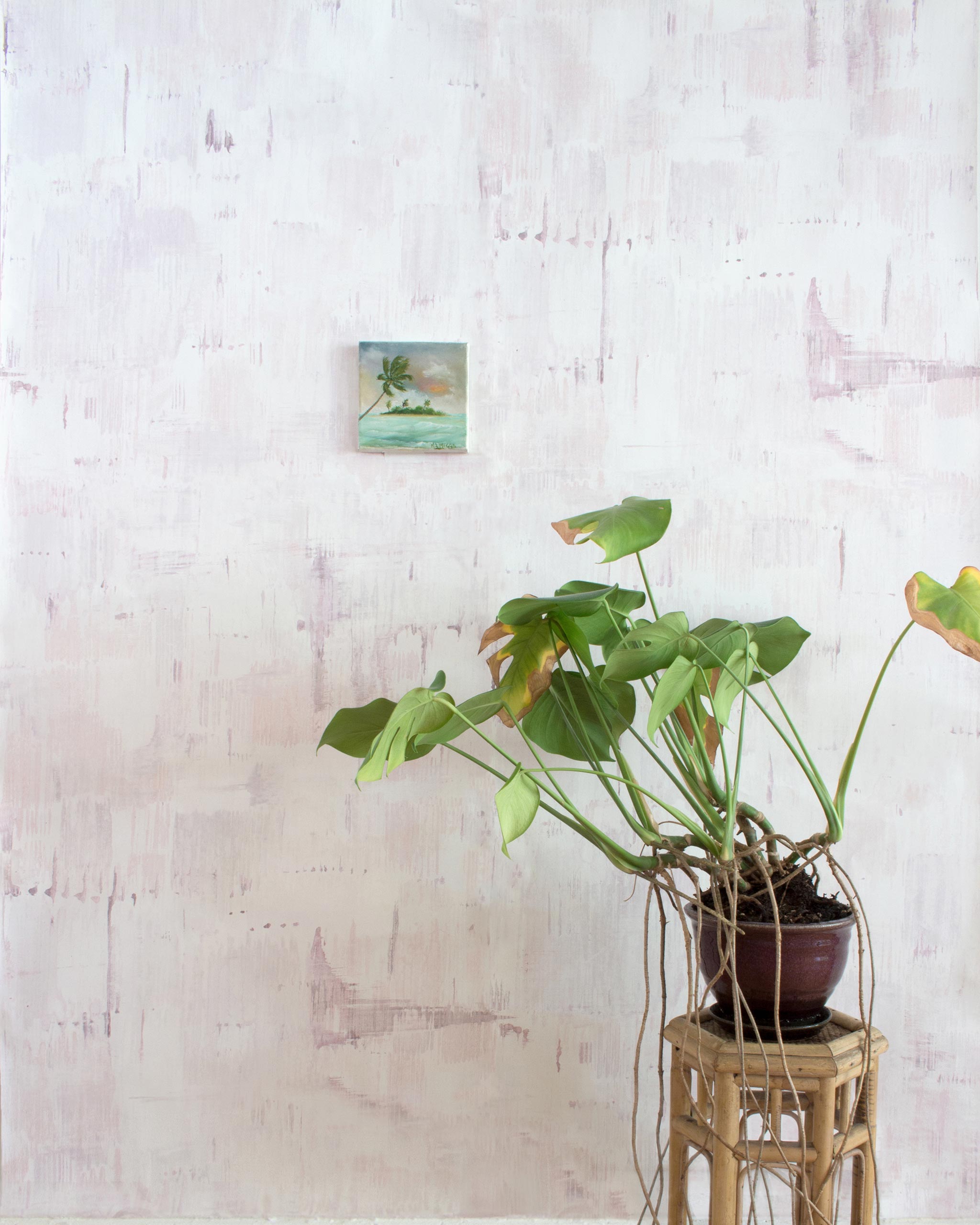 A potted plant on a stand in front of a wall papered in a watercolor textural print in shades of pink, cream and tan.
