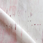 Detail of fabric in a watercolor paint blot print in light pink on a white field.