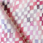 Detail of fabric in a painterly check pattern in shades of pink and purple on a white field.