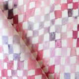 Detail of fabric in a painterly check pattern in shades of pink and purple on a white field.