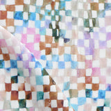 Detail of fabric in a painterly check pattern in shades of pink, brown and blue on a white field.