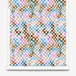 Partially unrolled wallpaper yardage in a painterly chess board print in a rainbow of shades on a white field.
