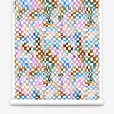 Partially unrolled wallpaper yardage in a painterly chess board print in a rainbow of shades on a white field.