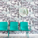 A row of turquoise chairs stands in front of a wall papered in a watercolor tree print in gray, turquoise and purple.