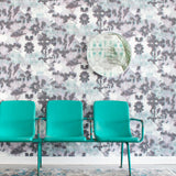 A row of turquoise chairs stands in front of a wall papered in a watercolor tree print in gray, turquoise and purple.