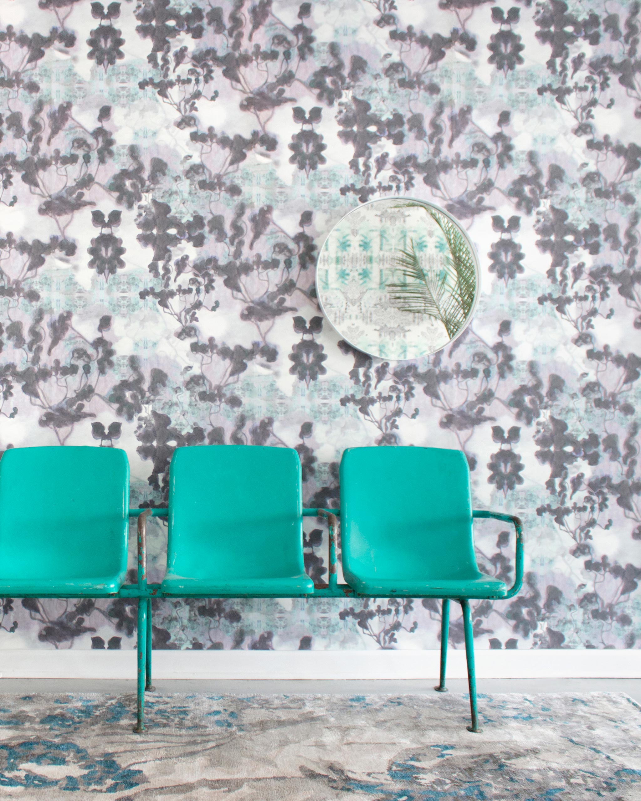 A row of turquoise chairs stands in front of a wall papered in a watercolor tree print in gray, turquoise and purple.