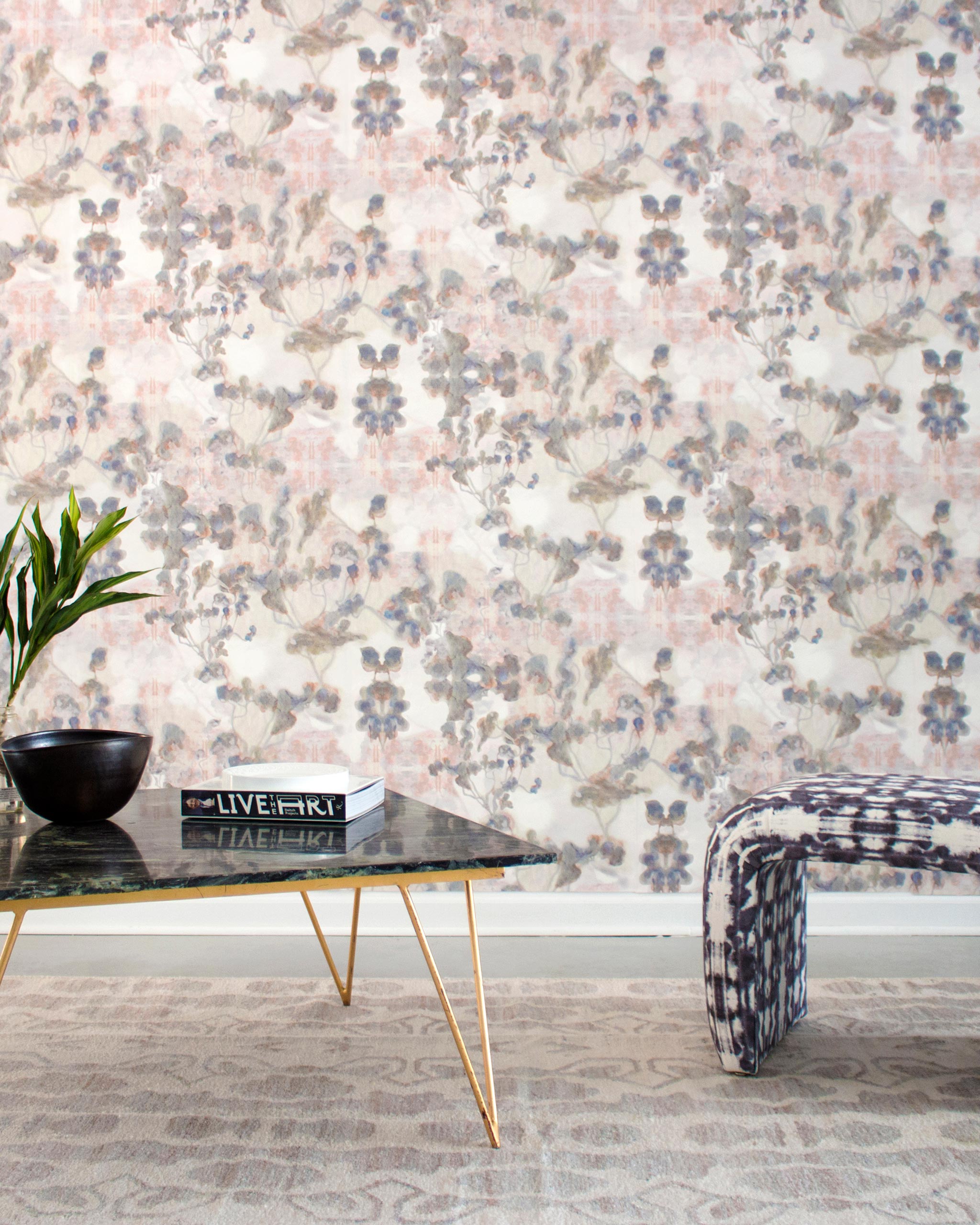 A modernist living tableau with a wall papered in a watercolor tree print in gray, peach, tan and white.